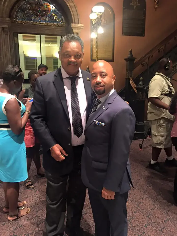 Cezar McKnight and another man pose at a formal event with a lively crowd.