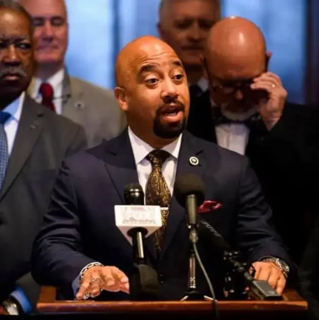 Cezar McKnight speaks at a podium, with formally dressed individuals behind him.