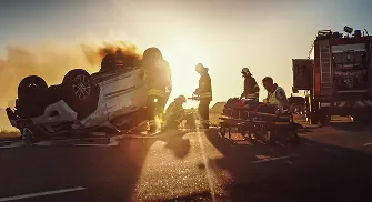 Emergency responders aid at a car crash with a flipped vehicle and smoke.